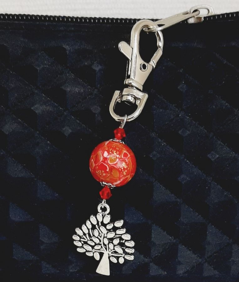 nyckelring i silver med symbol för livets träd och handgjord pärla i ljusrött och guld