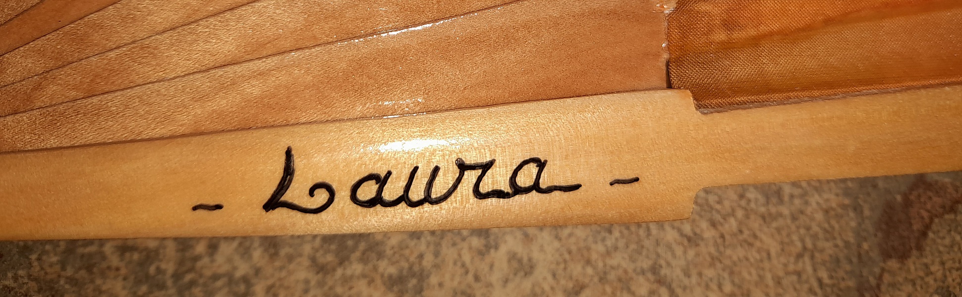 Signature artisanale peinte sur la branche d'un éventail en bois.