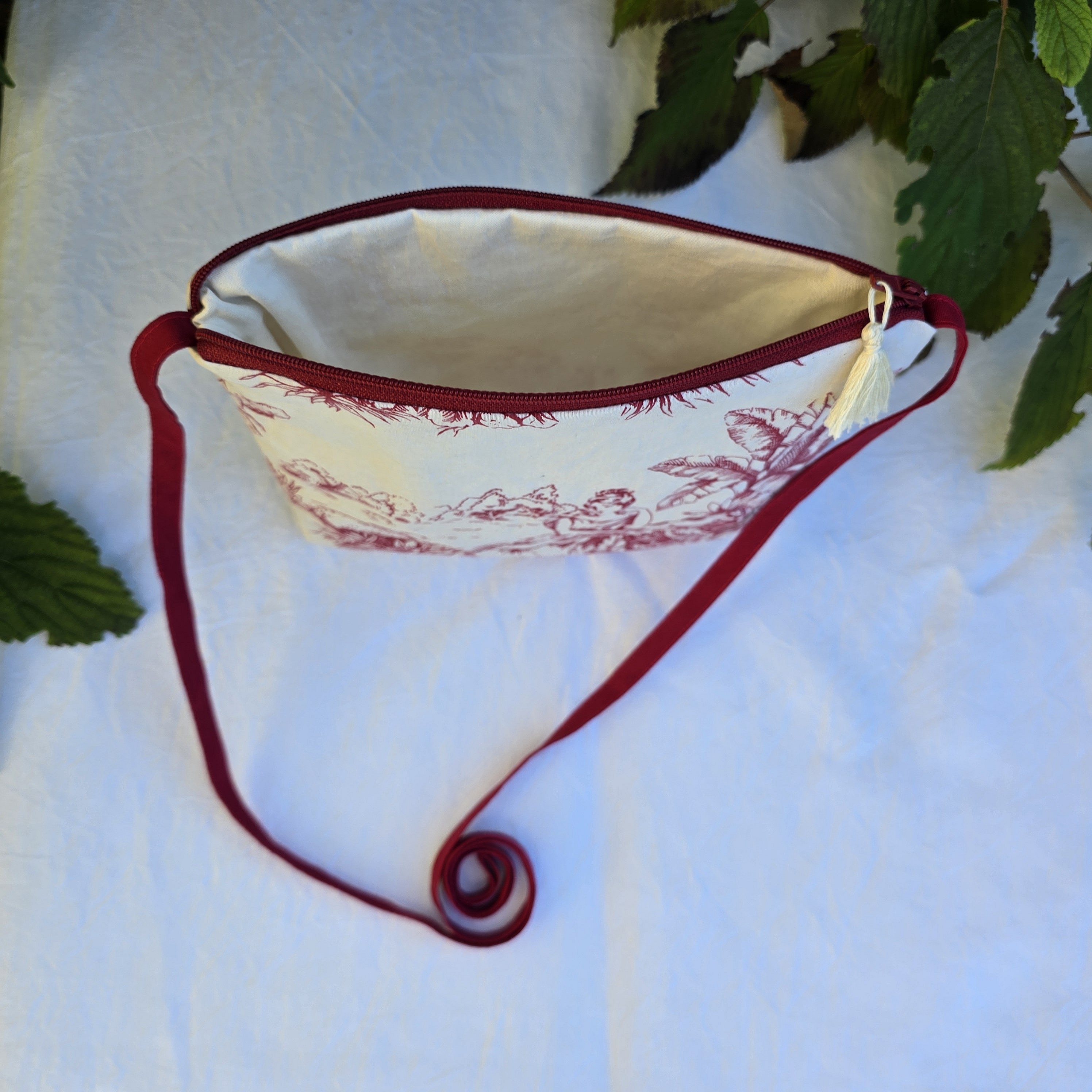 Pochette avec bandouli&egrave;re en tissu toile de Jouy bordeaux et &eacute;cru agr&eacute;ment&eacute;e d'un pompon