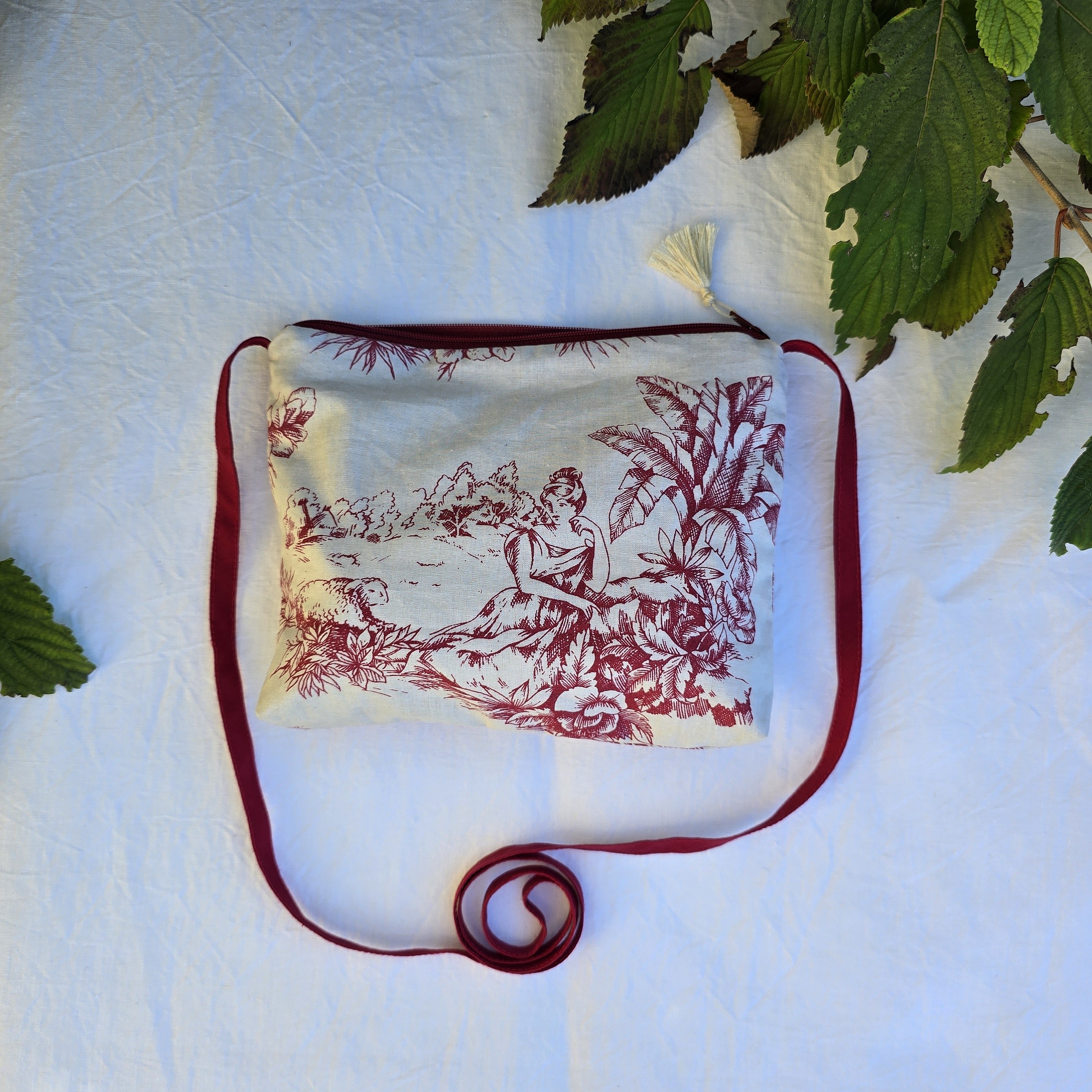 Pochette avec bandouli&egrave;re en tissu toile de Jouy bordeaux et &eacute;cru agr&eacute;ment&eacute;e d'un pompon