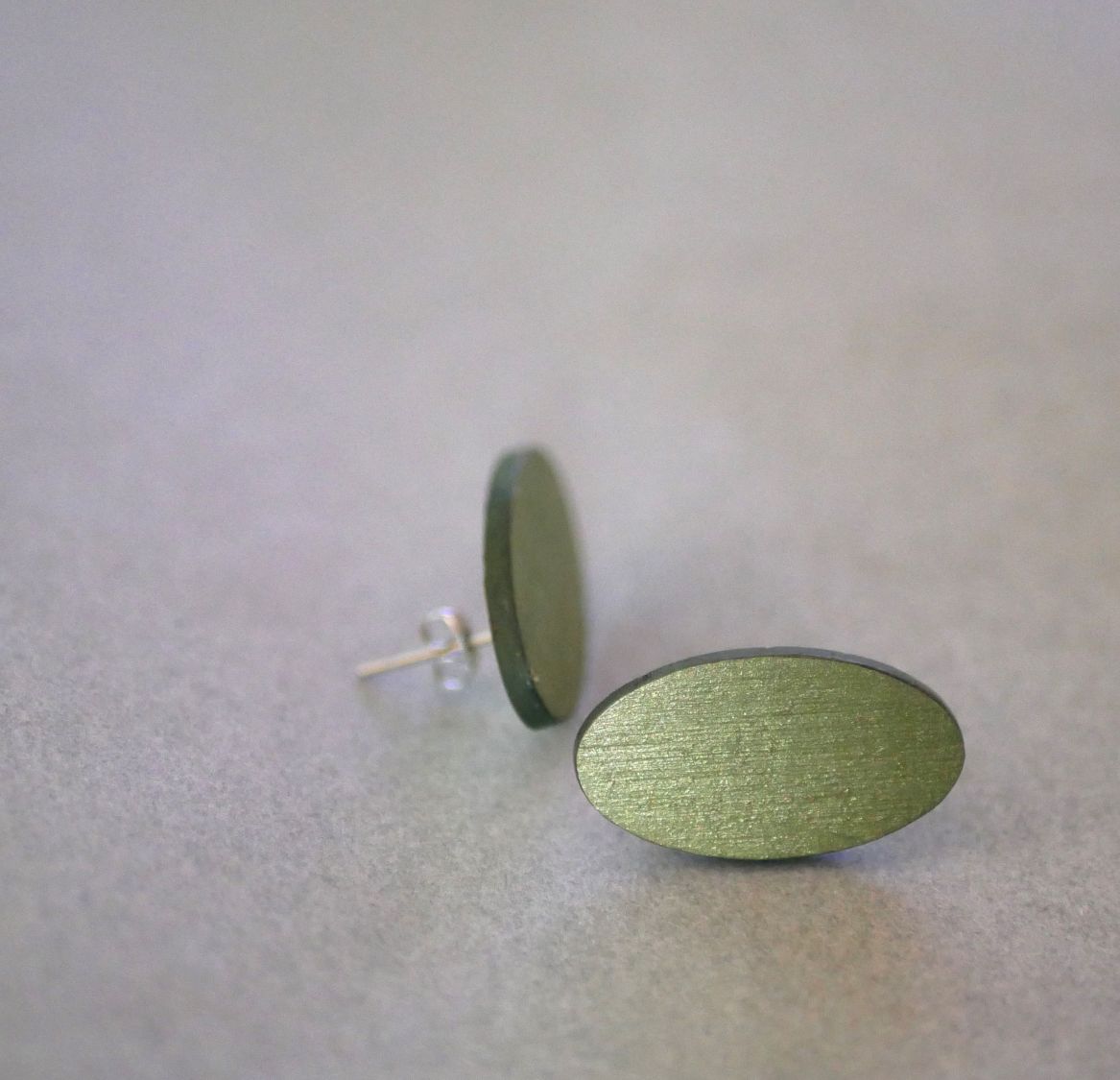 Ovala örhängen i trä målade i en duo av gröna färger med metallisk effekt.