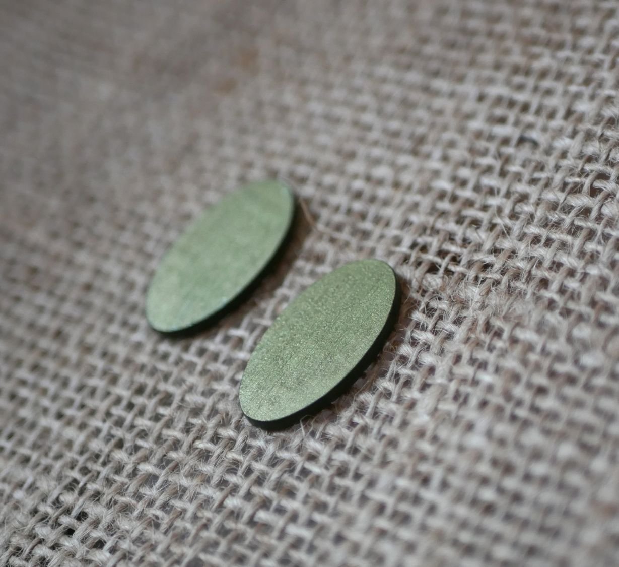 Ovala örhängen i trä målade i en duo av gröna färger med metallisk effekt.