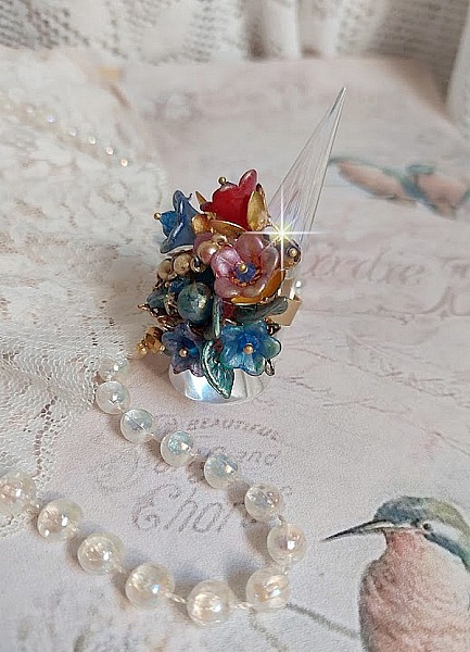 Bague Bel Air mont&eacute;e avec des fleurs lucites peintes &agrave; la main aux couleurs : Bleu, Rose, Rouge, Argent, Blanc avec feuilles ondul&eacute;es Vert Cuivr&eacute; &agrave; laquelle s&rsquo;ajoute perles Dor&eacute;es en Verre