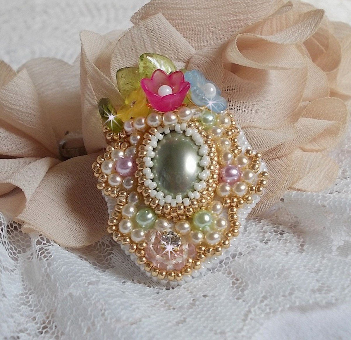 Envolée Fleurie ring broderad med en harts cabochon av Lucite blommor, pärlpärlor och fröpärlor.