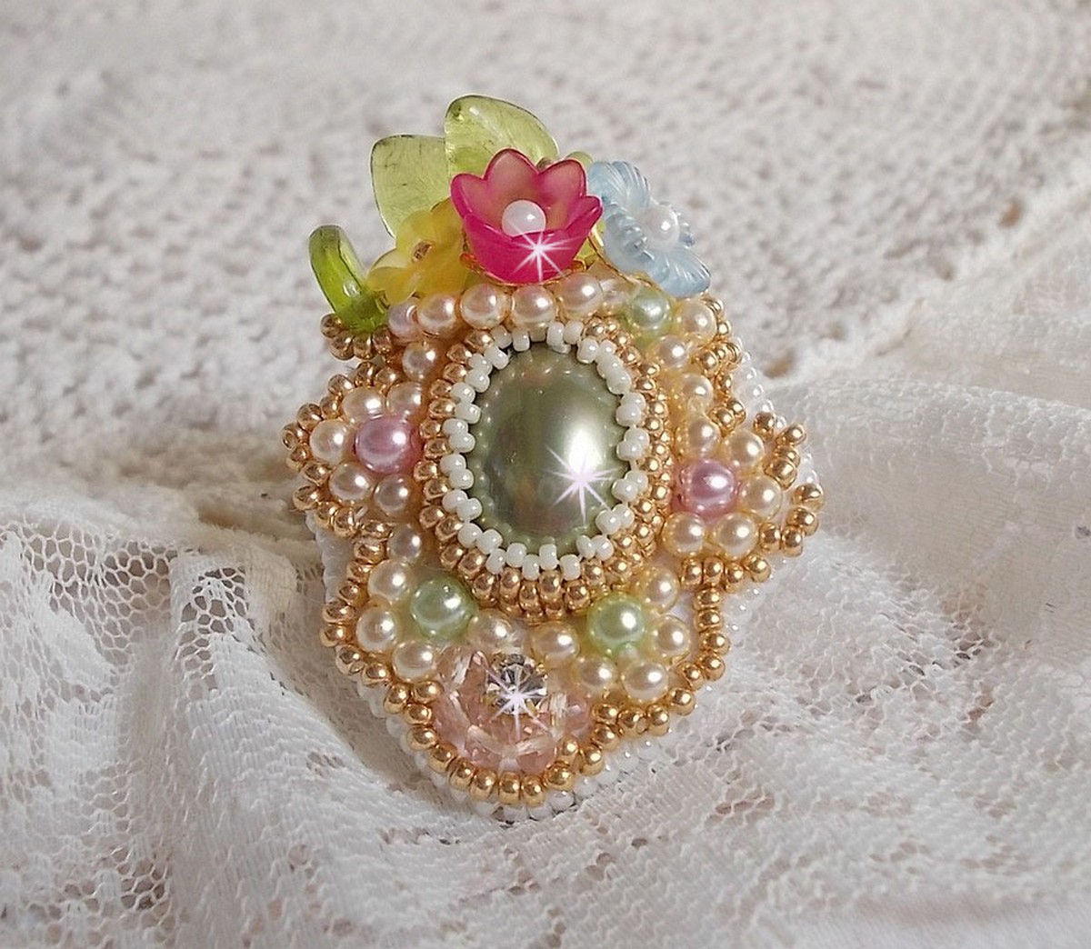 Envolée Fleurie ring broderad med en harts cabochon av Lucite blommor, pärlpärlor och fröpärlor.