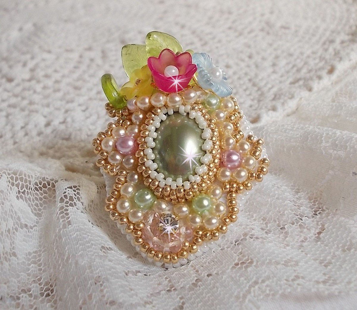 Envolée Fleurie ring broderad med en harts cabochon av Lucite blommor, pärlpärlor och fröpärlor.