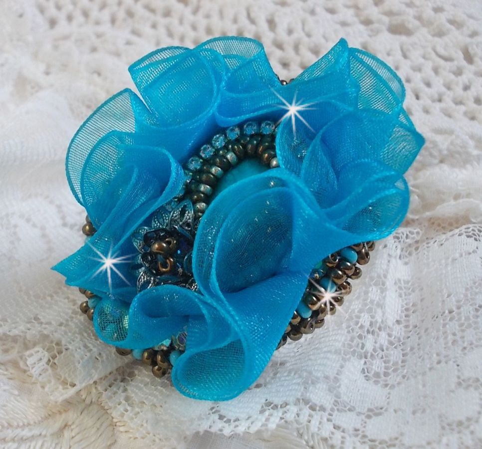 Ilycia Charmig ring broderad med en facetterad turkosblå harts cabochon och ett organza band.