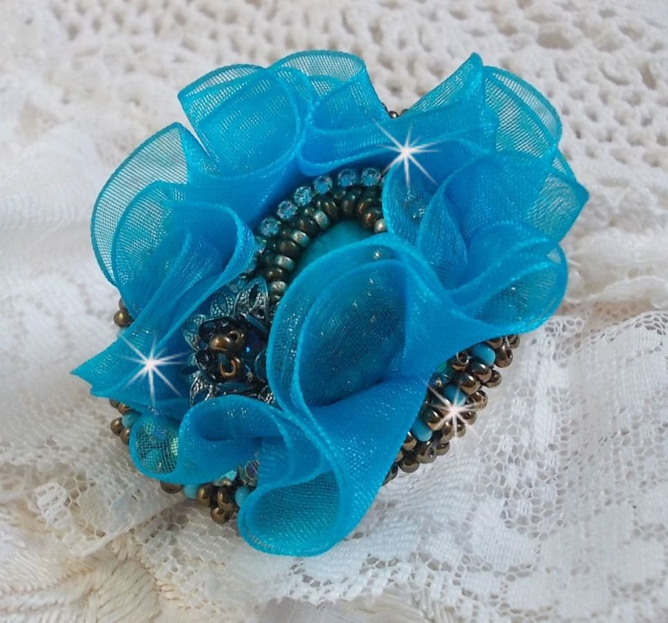 Ilycia Charmig ring broderad med en facetterad turkosblå harts cabochon och ett organza band.