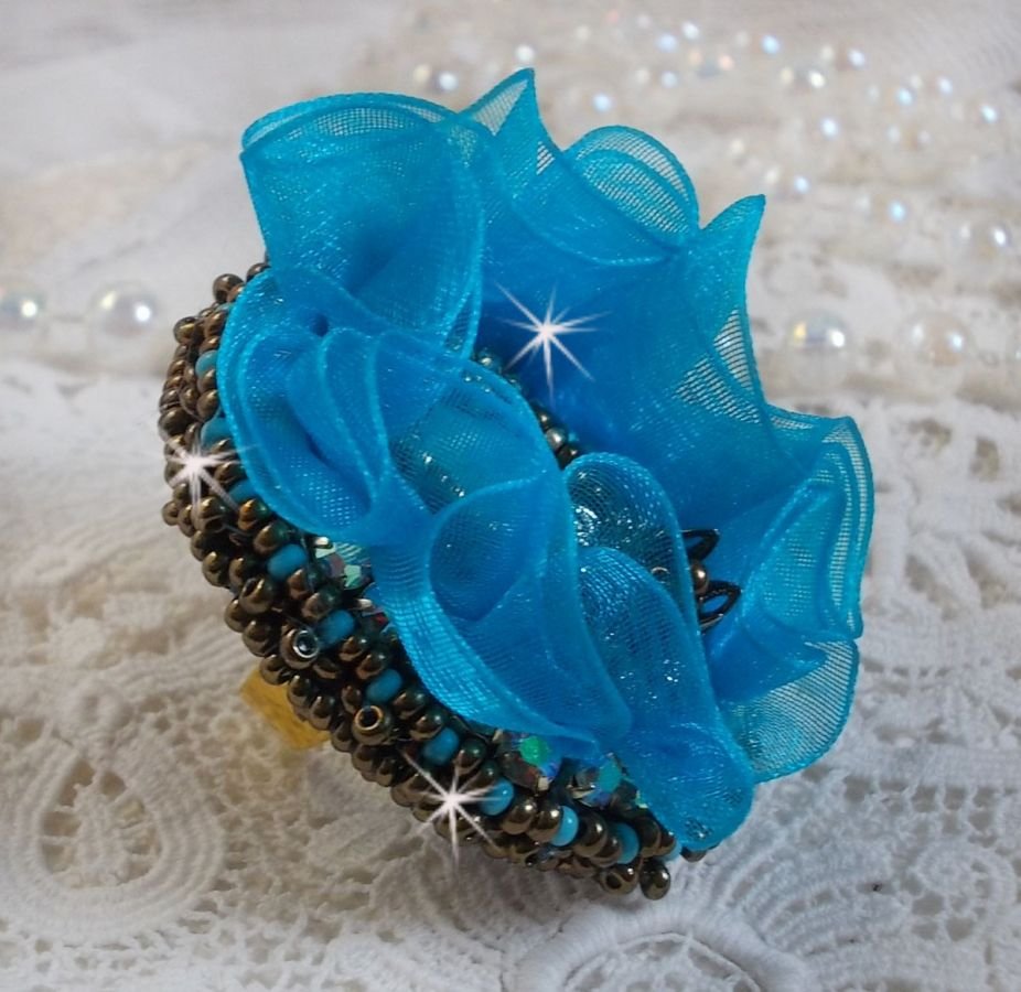 Ilycia Charmig ring broderad med en facetterad turkosblå harts cabochon och ett organza band.