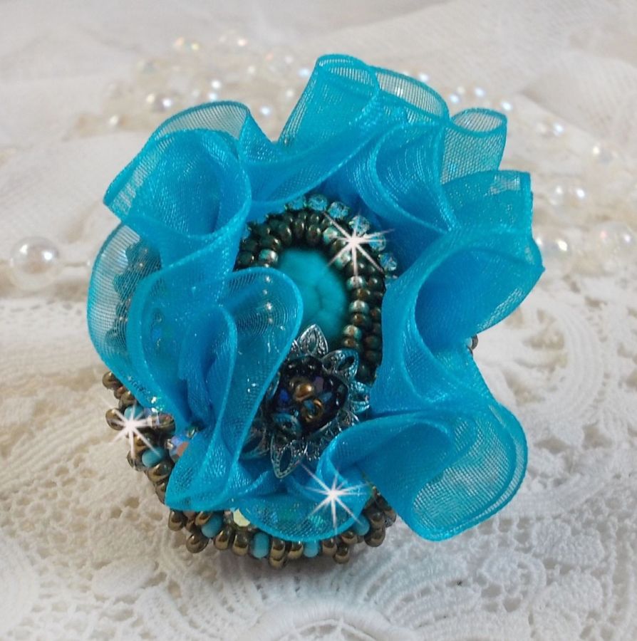 Ilycia Charmig ring broderad med en facetterad turkosblå harts cabochon och ett organza band.