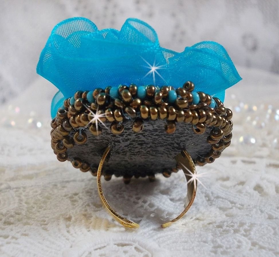 Ilycia Charmig ring broderad med en facetterad turkosblå harts cabochon och ett organza band.