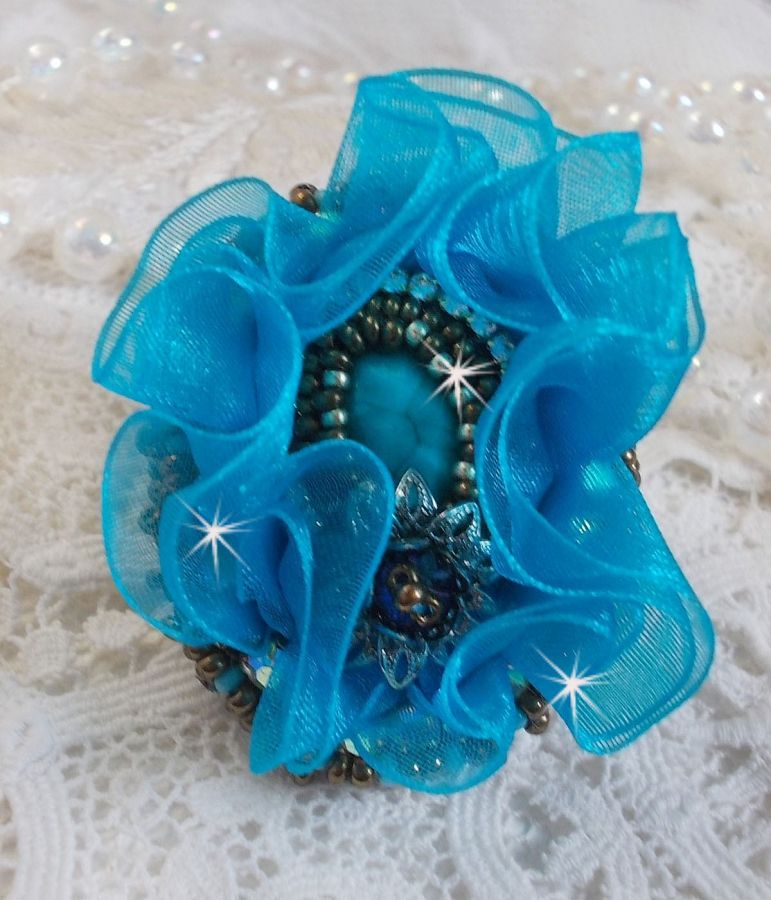 Ilycia Charmig ring broderad med en facetterad turkosblå harts cabochon och ett organza band.