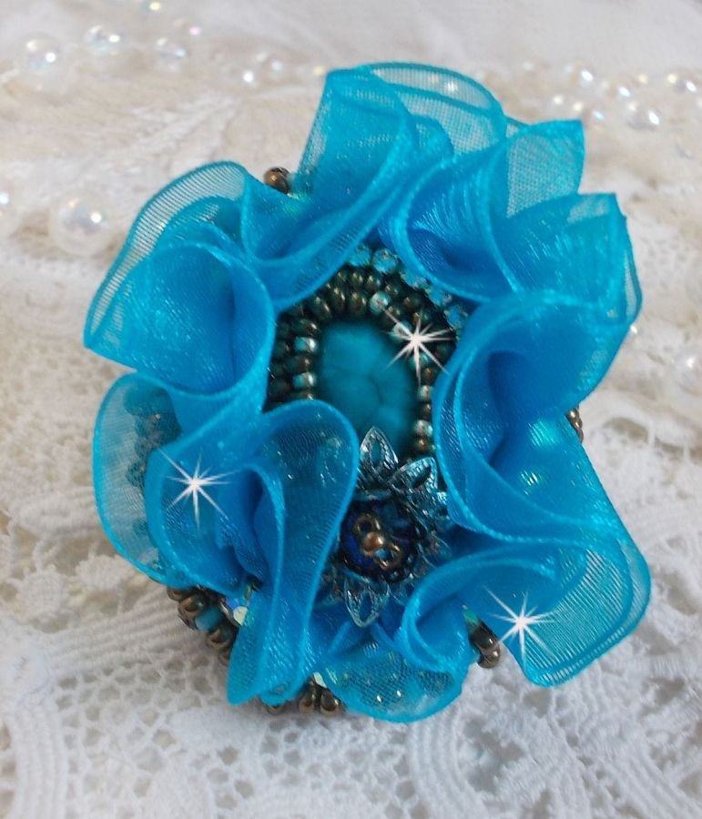 Ilycia Charmig ring broderad med en facetterad turkosblå harts cabochon och ett organza band.