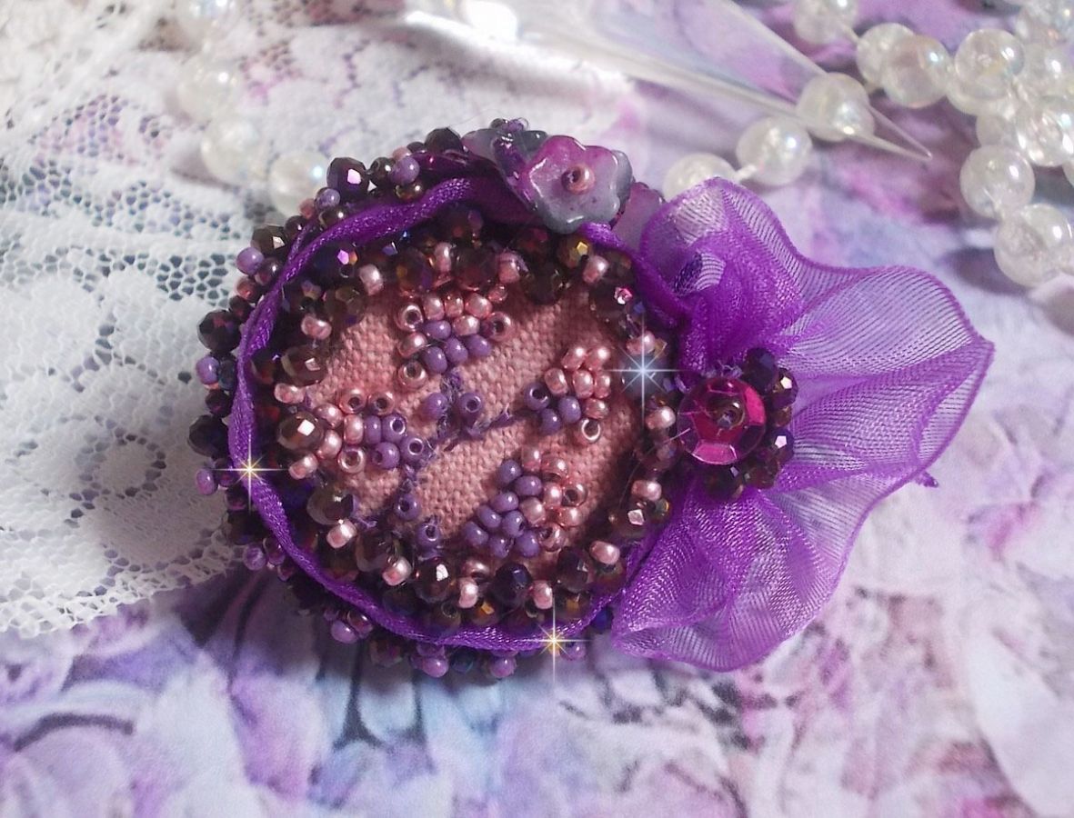 Romantisk Lady Ring broderad på ett rosa linnetyg med rosa, iris, lila och persika pärlor. 