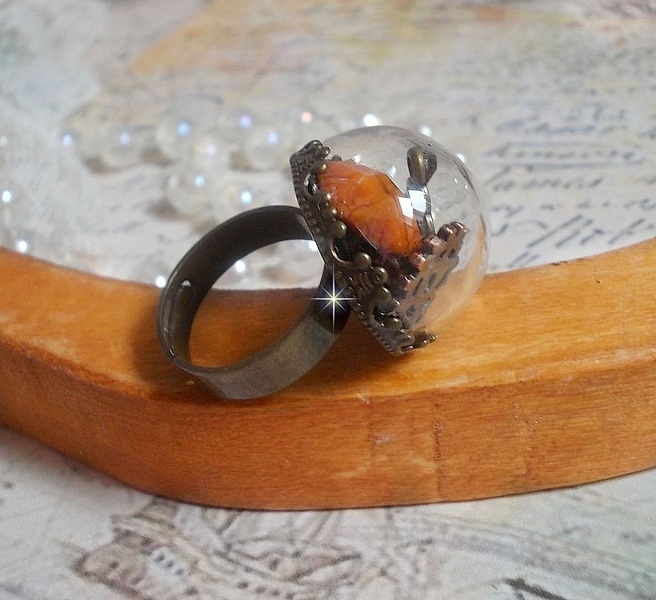 Bague Majest&eacute; Steampunk aux rouages m&eacute;caniques &agrave; laquelle s&rsquo;ajoute une cl&eacute; et un strass de couleur Siam et un strass en verre Dor&eacute;. Le tout est mis sous un globe en verre sur une bague r&eacute;glable laiton