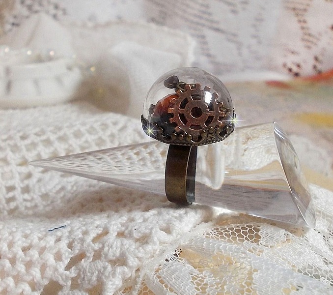 Bague Majest&eacute; Steampunk aux rouages m&eacute;caniques &agrave; laquelle s&rsquo;ajoute une cl&eacute; et un strass de couleur Siam et un strass en verre Dor&eacute;. Le tout est mis sous un globe en verre sur une bague r&eacute;glable laiton