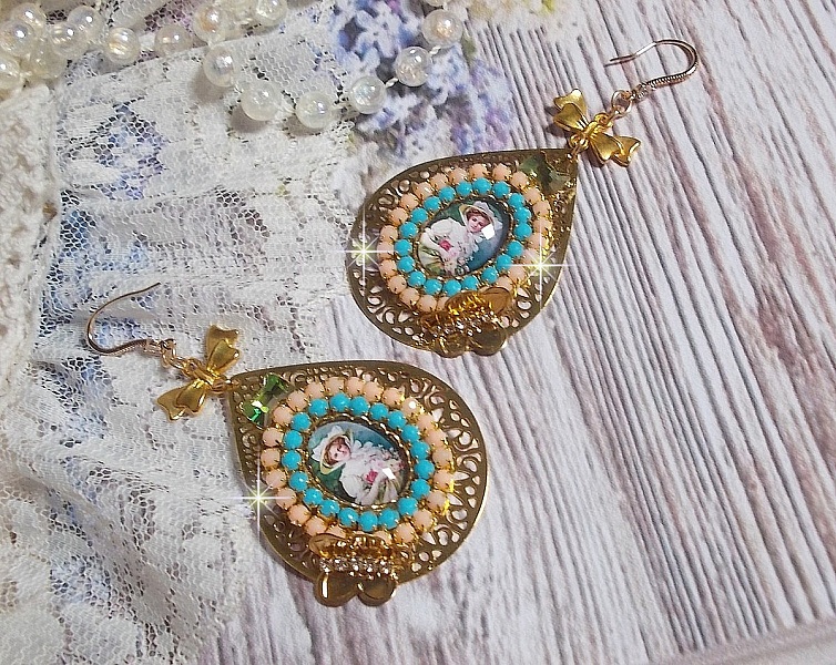 BO Mademoiselle Noellia avec des cabochons ovales repr&eacute;sentant une femme avec un chapeau et un n&oelig;ud blanc &agrave; laquelle s&rsquo;ajoute des cristaux, cha&icirc;nes strass P&ecirc;che et Turquoise sur crochets en plaqu&eacute; Or