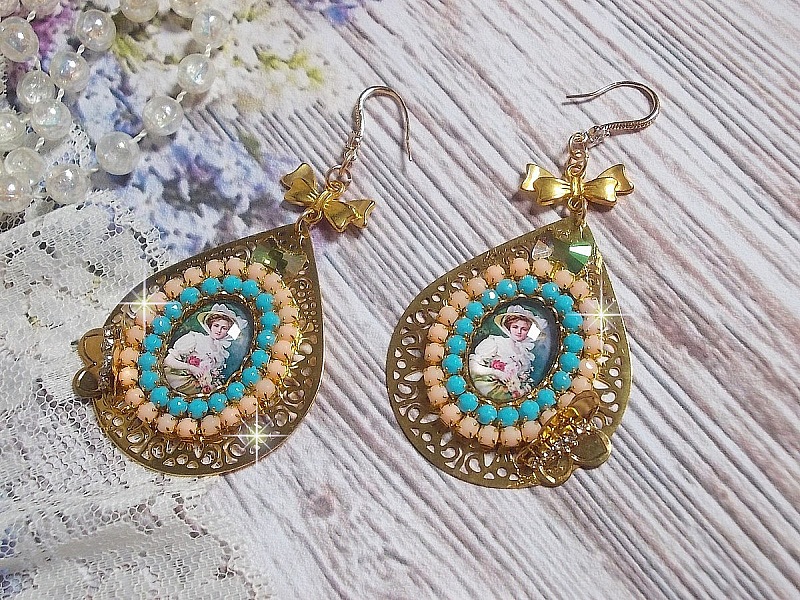 BO Mademoiselle Noellia avec des cabochons ovales repr&eacute;sentant une femme avec un chapeau et un n&oelig;ud blanc &agrave; laquelle s&rsquo;ajoute des cristaux, cha&icirc;nes strass P&ecirc;che et Turquoise sur crochets en plaqu&eacute; Or