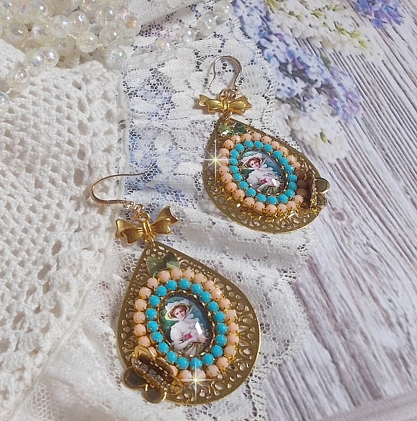 BO Mademoiselle Noellia avec des cabochons ovales repr&eacute;sentant une femme avec un chapeau et un n&oelig;ud blanc &agrave; laquelle s&rsquo;ajoute des cristaux, cha&icirc;nes strass P&ecirc;che et Turquoise sur crochets en plaqu&eacute; Or