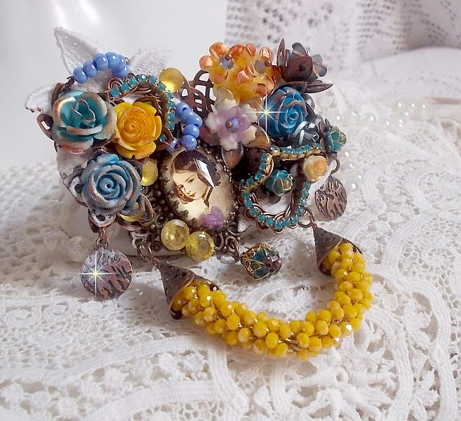Broche Eclats P&eacute;tillants d&rsquo;inspiration Baroque, orn&eacute;e de fleurs en r&eacute;sine autour d&rsquo;un cabochon strass&eacute;s et perl&eacute;s sur estampes, cristaux, breloques, perle cloisonn&eacute;e, perles jaunes en verre et roses. 