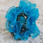Ilycia Charmig ring broderad med en facetterad turkosblå harts cabochon och ett organza band.