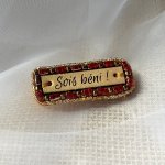 Broche à message en cuir gravé 'sois béni' en perles rouges et dorées 
